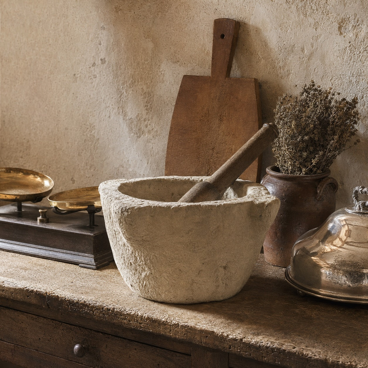 Antique French kitchen décor with marble mortar and pestle, rustic cutting board, vintage mercantile scales, and silver meat dome on a worn stone counter in a French country kitchen