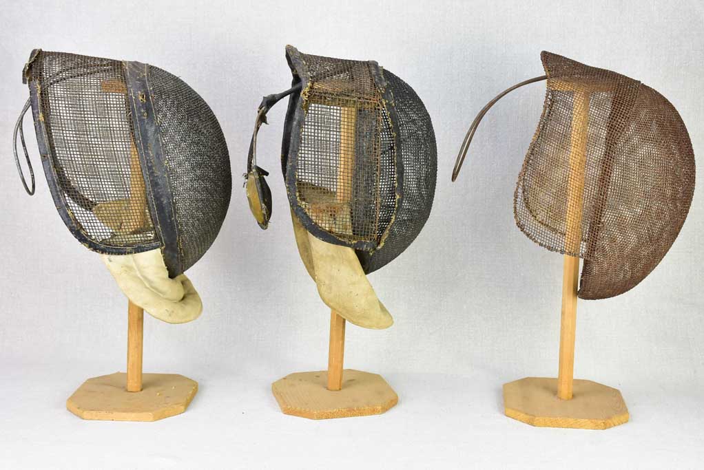 Collection of three antique French fencing masks on vintage hat stands