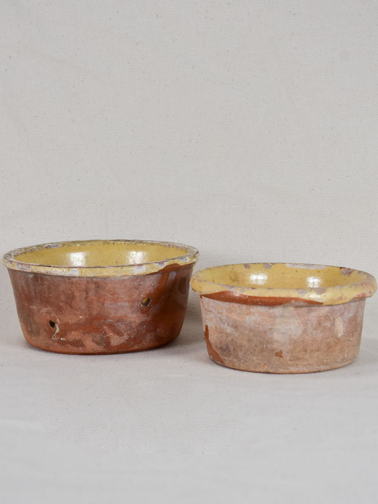Two antique French clay cheese strainers with timeworn yellow glaze