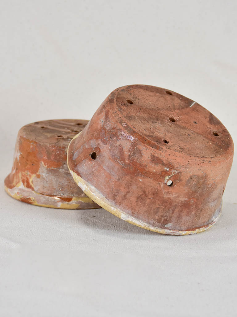 Two antique French clay cheese strainers with timeworn yellow glaze