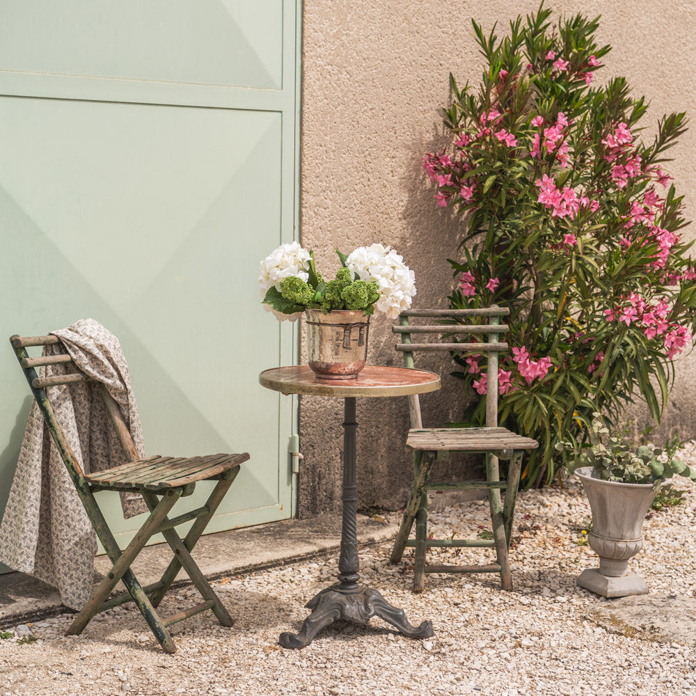 Antique French bistro table with weathered folding chairs in a Provençal courtyard