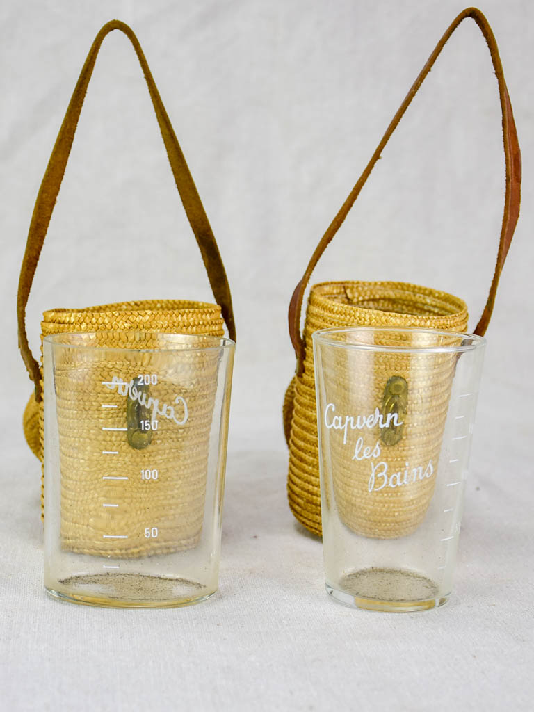 Two mid century French 'verre de cure' glasses in baskets