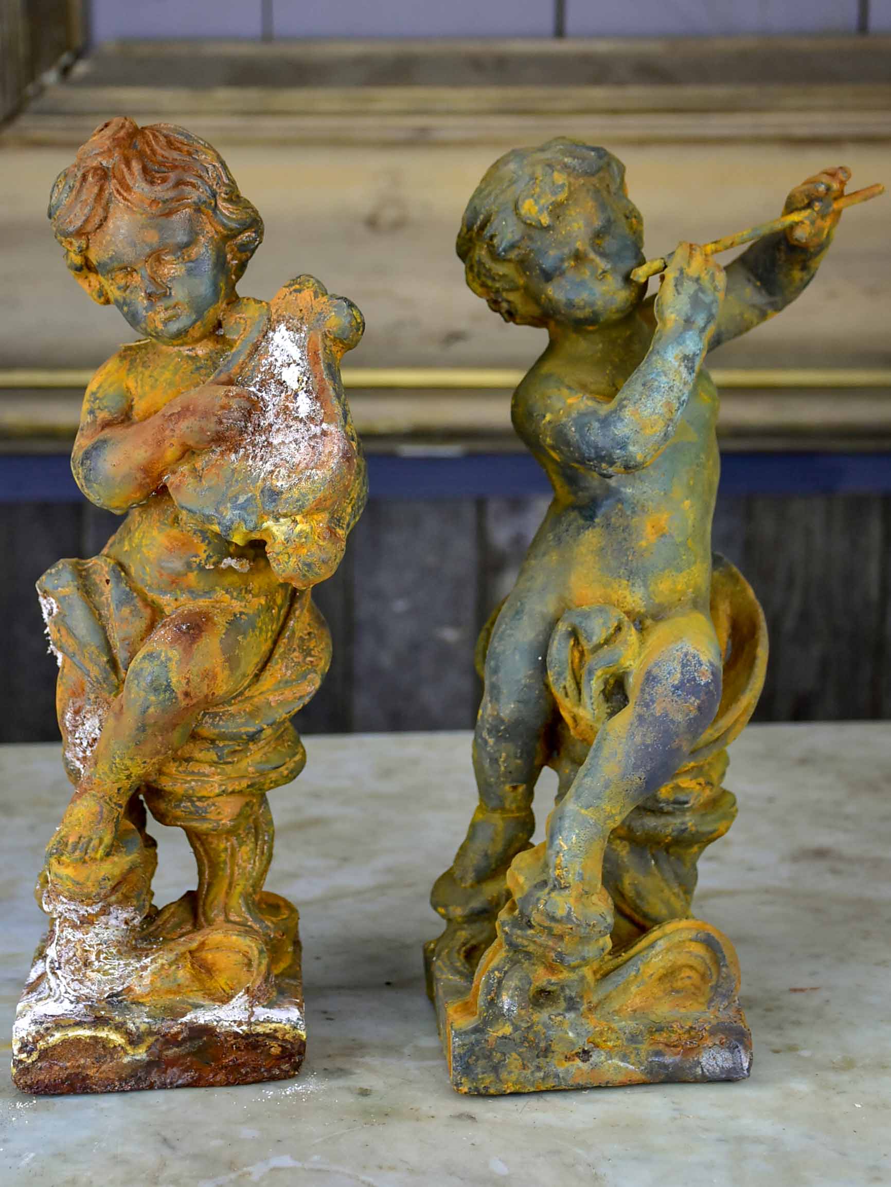Two antique cast iron cherubs playing musical instruments