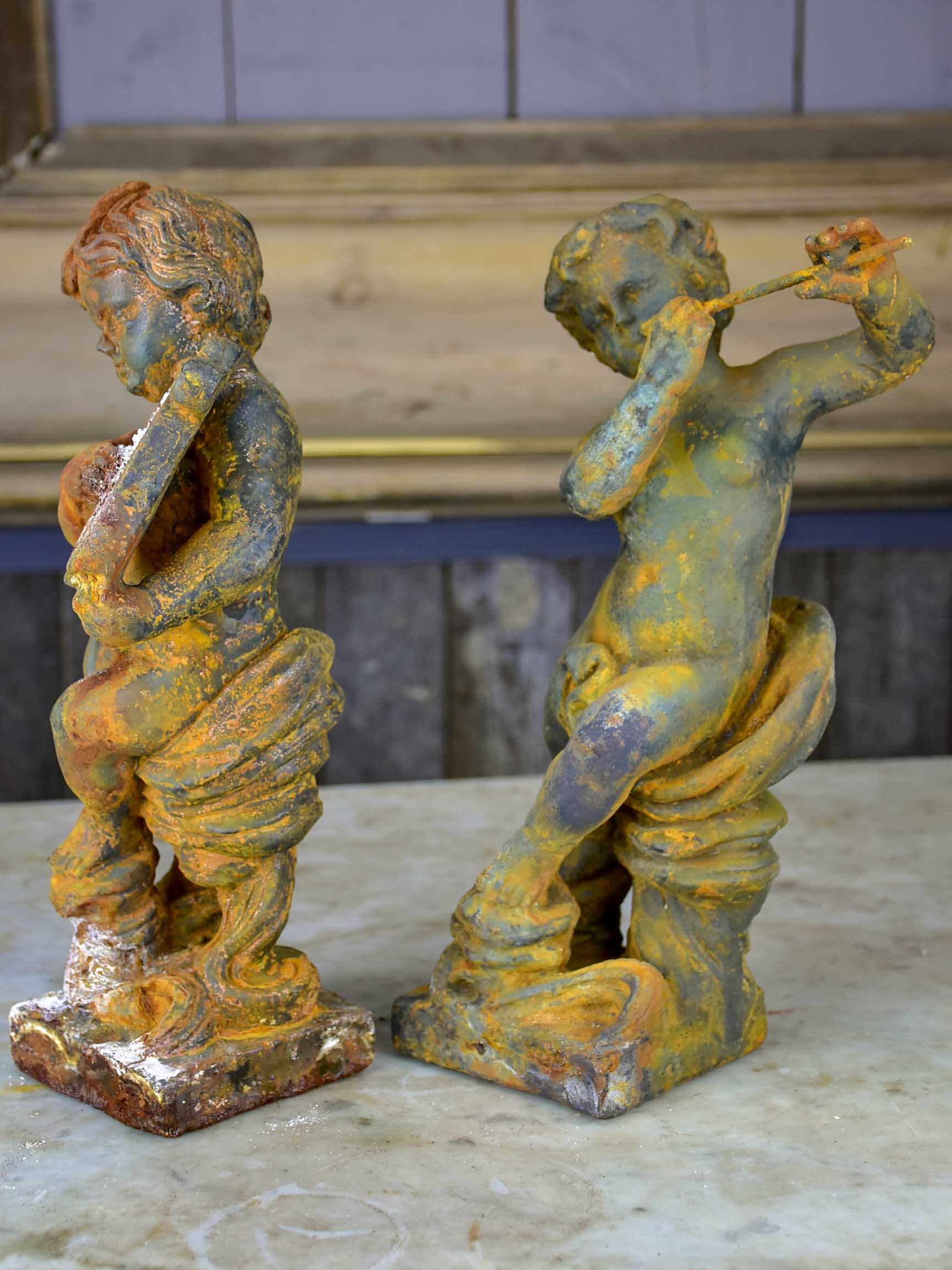 Two antique cast iron cherubs playing musical instruments