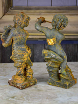 Two antique cast iron cherubs playing musical instruments