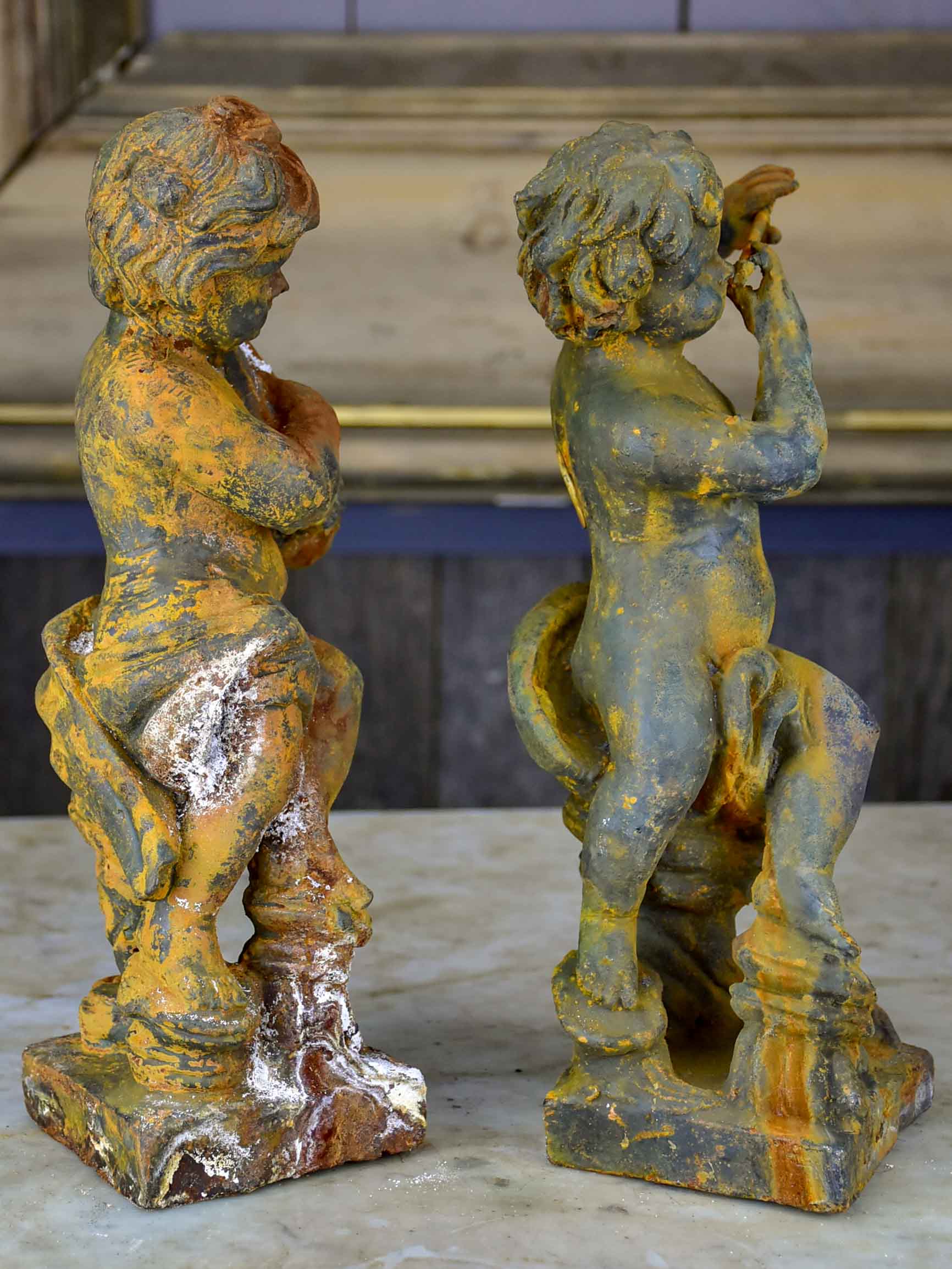 Two antique cast iron cherubs playing musical instruments