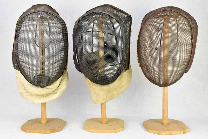 Collection of three antique French fencing masks on vintage hat stands